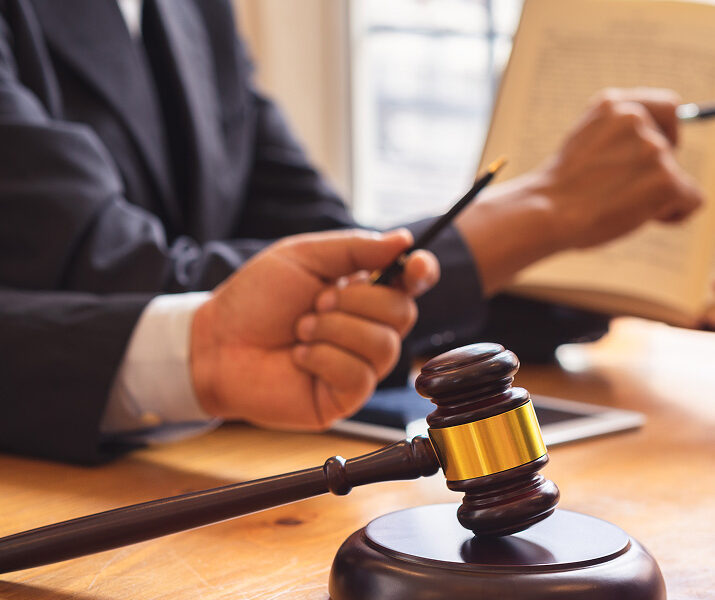 Judge reviewing legal documents with gavel on desk in courtroom setting.