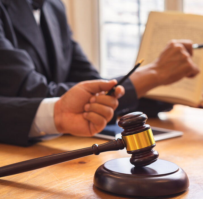 GettyImages-1034233010 1 Judge reviewing legal documents with gavel on desk in courtroom setting.