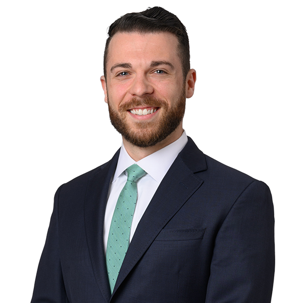 Smiling man in a suit and green tie with beard, standing against a white background.
