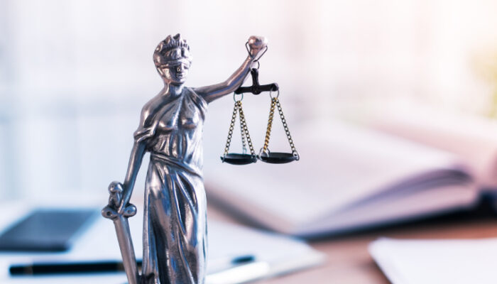 Lady Justice statue on a desk with open books and scales, symbolizing law and fairness in a professional setting.